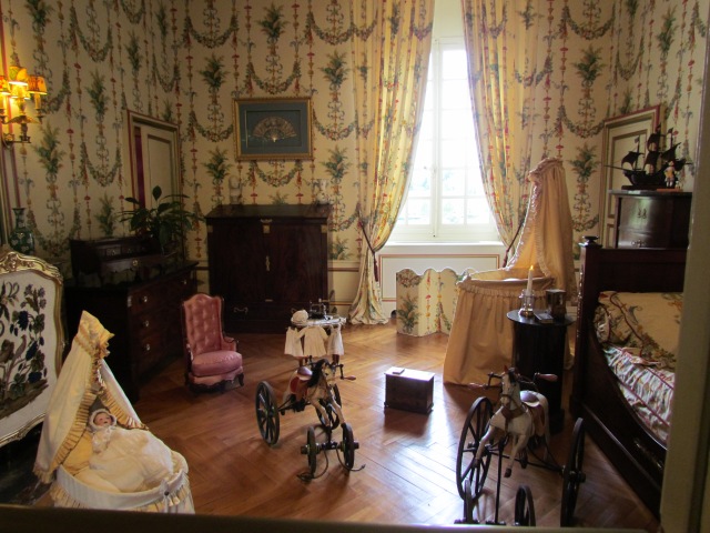 This beautiful nursery has matching wallpaper, drapes and bedspread. In the foreground are the first rocking horses from the time of Napoleon III.